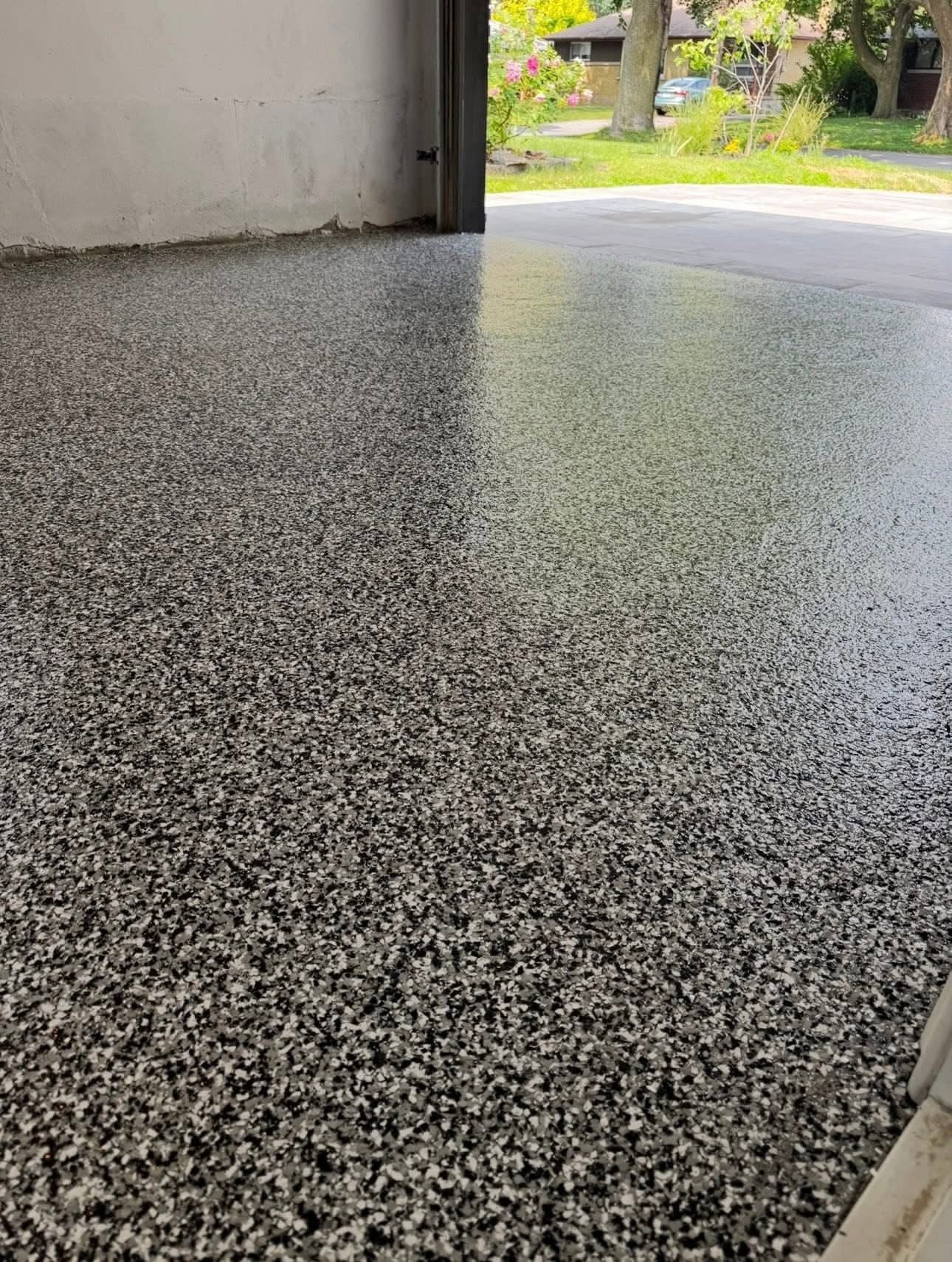 High-gloss black flake epoxy garage floor with the door open to a yard